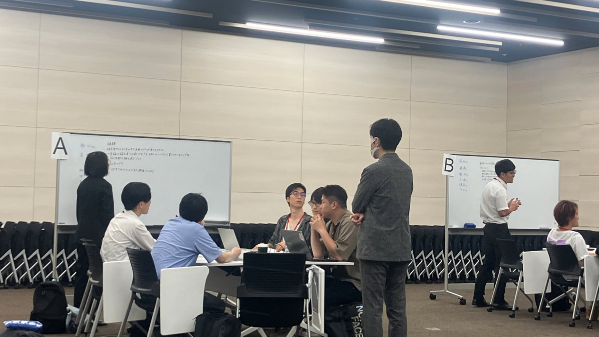 グループディスカッションの様子。ホワイトボードを前に、複数の参加者がDXやAI活用の課題について意見交換をしている。